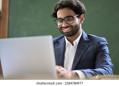 Smiling Indian Young Business Man Executive, Company Manager, Online Teacher Professor Or Office Employee Worker Wearing Suit And Eyeglasses Working On Laptop Looking At Computer Sitting At Work