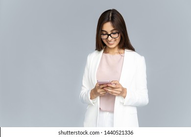 Smiling Indian Young Business Woman Wear White Suit Glasses Using Smartphone App Isolated On Grey Background Copy Space, Happy Hindu Girl Holding Looking At Mobile Phone Texting Chat On Cellphone