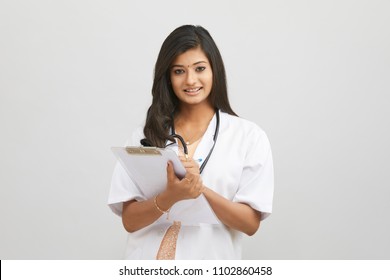 Smiling Indian young female doctor writing in clipboard