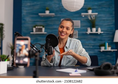 Smiling Influencer Recording Mouse Review With Smartphone. Content Creator In Home Studio With Microphone And Mobile Phone Doing Product Recommendation. Vlog Podcast For Social Media.