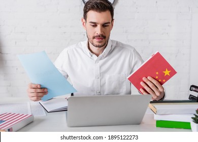 Smiling Interpreter Holding Chinese Dictionary And Document Near Laptop In Translation Agency