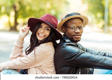 Smiling interracial couple in hats sitting back to back