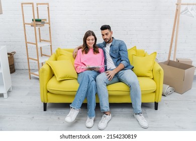 Smiling Interracial Couple Holding Color Palette On Couch At Home