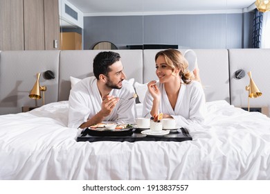 Smiling interracial couple looking at each other near breakfast on tray on hotel bed - Powered by Shutterstock