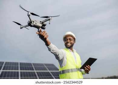 Smiling interracial electrical engineer with tablet in hand catching drone at solar panels field.