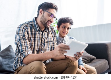 smiling jewish father and son using digital tablet in apartment 
