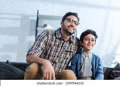smiling jewish father and son watching tv in apartment 