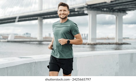 Smiling jogger running by the waterfront with urban bridge backdrop, embodying an active lifestyle. - Powered by Shutterstock