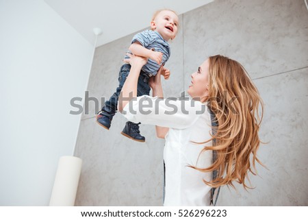 Smiling joyful young mother playing and having fun with her little son at home