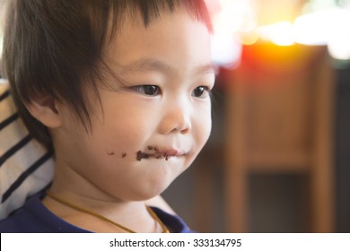 Smiling Kid Eating Chocolate At Coffee Shop With His Mom. Smeared Stained With Chocolate Lips