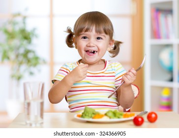 Smiling Kid Girl Eating Healthy Vegetables At Kitchen