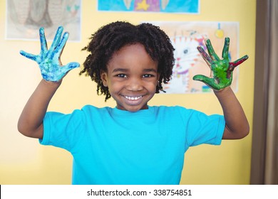 Smiling kid holding up his hands covered in paint