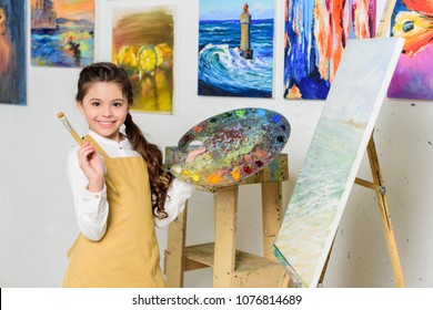 Smiling Kid Holding Painting Brush And Canvas In Workshop Of Art School