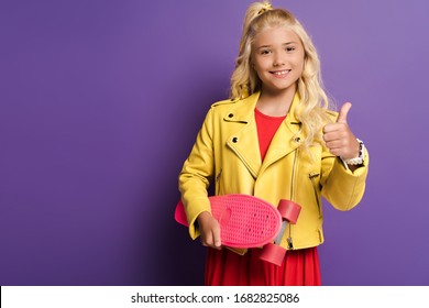 Smiling Kid Holding Penny Board And Showing Like On Purple Background