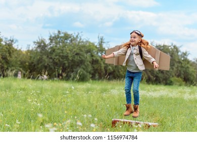 Smiling Kid In Pilot Costume Jumping From Retro Suitcase In Summer Field