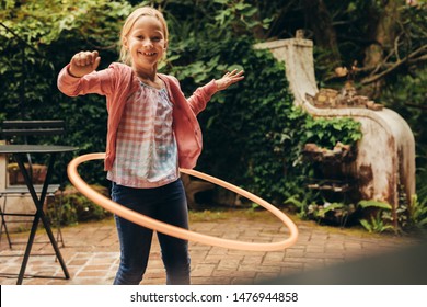 Smiling Kid Playing With A Hula Hoop In Her Backyard. Girl Having Fun Turning A Hoopla Ring Around Her Waist.