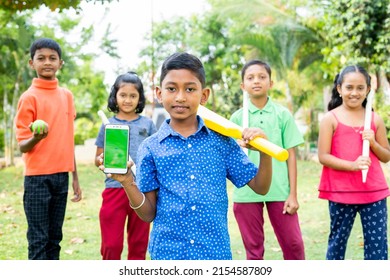 Smiling kid showing green screen mobile phone with cricket bat by looking at camera with friends at park - concept of training, advertisement and promotion - Powered by Shutterstock