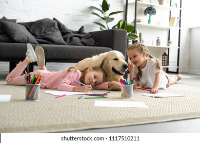 Smiling Kids Lying On Floor Together With Golden Retriever Dog At Home