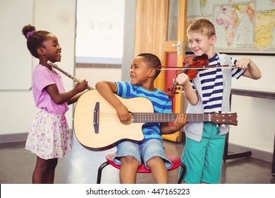 Smiling kids playing guitar, violin, flute in classroom at school