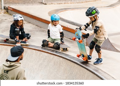 Smiling Kids Wearing Safety Gear Having A Skateboarding Lesson With A Teacher At The Skate Ramp