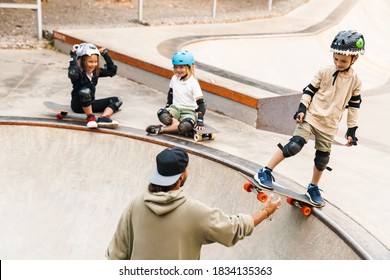 Smiling Kids Wearing Safety Gear Having A Skateboarding Lesson With A Teacher At The Skate Ramp