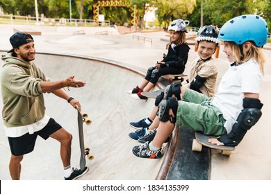 Smiling Kids Wearing Safety Gear Having A Skateboarding Lesson With A Teacher At The Skate Ramp