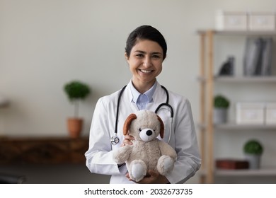 Smiling Kind Young Indian Ethnic Female General Practitioner Pediatrician Holding Fluffy Toy Teddy Bear In Hands, Waiting For Small Patients, Professional Friendly Approach To Children Concept.