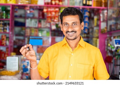 Smiling Kirana Or Grocery Merchant Showing Credit Card By Looking At Camera At Grocery Shop - Concept Of Credit Card Payment, Shopping And Small Business.