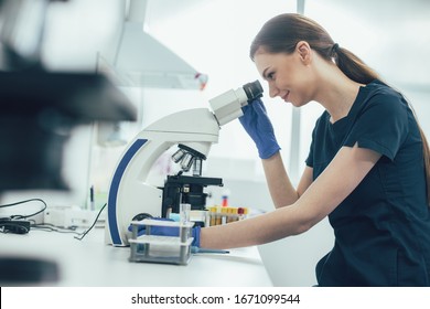 Smiling lab assistant working with samples and using a microscope in her laboratory - Shutterstock ID 1671099544