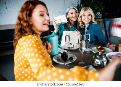 Smiling lady making selfie while sitting at the table with two elegant joyful women stock photo