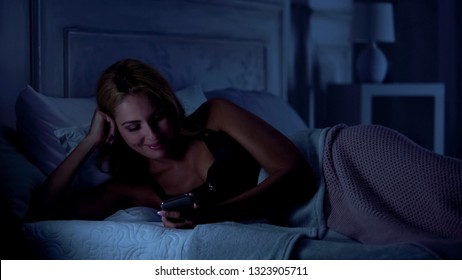 Mujer sonriente viendo videos graciosos en internet, divirtiéndose antes de dormir