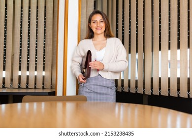 Smiling Latin American Business Woman Standing In Modern Office Interior, Holding Briefcase With Papers, Ready For Partner Meeting.