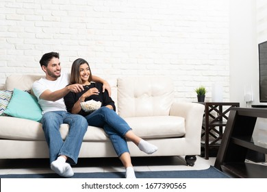 Smiling Latin Couple Watching TV While Relaxing On Sofa In Living Room At Home