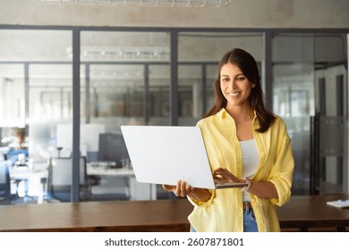 Gerente de marketing feminino hispânico latino sorridente, especialista em ti profissional trabalhando, navegando no computador laptop em pé no local de trabalho no escritório. Jovem funcionária usando pc para negócios. Copiar espaço