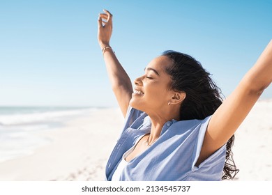 Smiling latin hispanic woman stretching hand and relaxing on beach. Woman breathing deeply at seaside with eyes closed. Happy woman standing on the beach and enjoy the sun tan with arms outstretched. - Shutterstock ID 2134545737