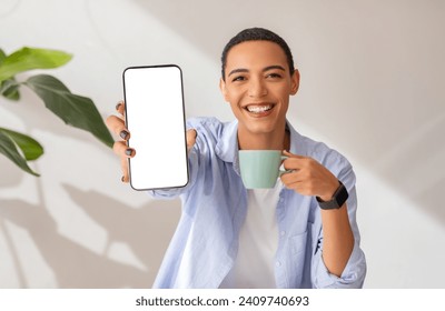 Smiling latin woman showing a blank smartphone screen while holding a coffee mug, wearing a blue shirt and smartwatch, in a bright room with houseplants, ad, offer and sale - Powered by Shutterstock