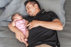 Smiling Latino Father Lying Down Babysitting Sleeping Daughter