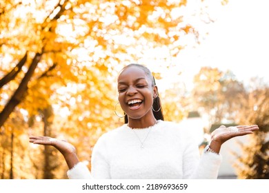 Smiling Laughing African American Woman Standing In The City Park, Having Fun With Stretched Hands. Autumn Season, Yellow Red And Orange Leaves. Fall Time.

