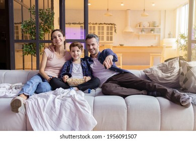 Smiling laughing parent showing funny video to son on television. Parent and son watching comedy movie on tv-set at home. Happy family sitting on comfort sofa. Cozy evening in living room interior