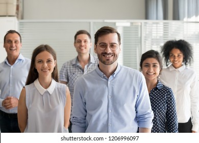 Smiling leader ceo or professional business coach looking at camera posing in office with diverse happy team at background, successful startup founder, corporate employee with staff members portrait