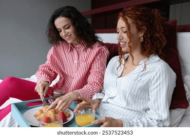 Smiling lesbian couple enjoying breakfast on bed - Powered by Shutterstock