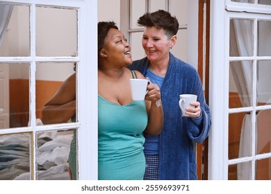 Smiling lesbian couple enjoying coffee by window - Powered by Shutterstock