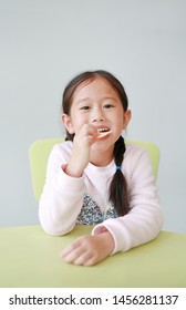 Smiling Little Asian Child Girl Eating Crispy Potato Chips On White Background. Kid Enjoy Eating Concept.