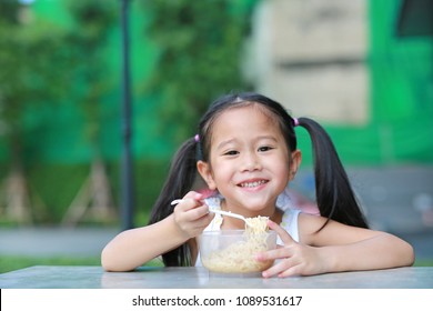 Smiling Little Asian Kid Girl Eating Instant Noodles In The Morning At The Garden.