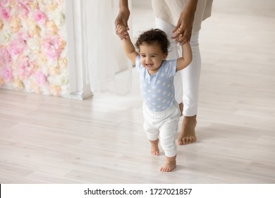 Smiling Little Biracial Toddler Infant Child Make First Steps At Home Holding Mom Hands, Happy Small African American Baby Learn Walking With Mother Support And Care, Upbringing, Childcare Concept