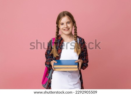 Smiling little blonde girl 10-12 years old in school uniform with backpack holding books isolated on pastel pink background studio portrait. The concept of children's lifestyle. Education at school.