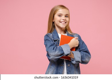 Smiling little blonde kid girl 12-13 years old in denim jacket isolated on pastel pink background children studio portrait. Childhood lifestyle concept. Mock up copy space. Holding book, notebook