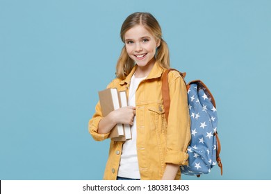 Smiling little blonde kid girl 12-13 years old wearing yellow jacket with backpack hold books isolated on pastel blue background studio portrait. Childhood lifestyle concept. Education in school.