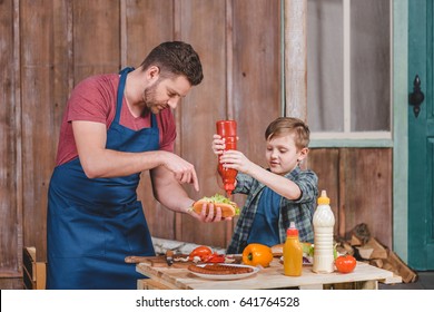 Smiling Little Boy With Father Cooking Hot Dog At Backyard, Dad And Son Cooking Concept