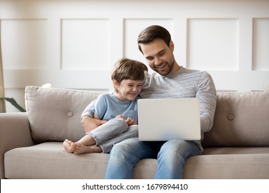 Smiling little boy relax on couch at home with young dad watch funny videos on laptop together, overjoyed father rest with preschooler son in living room, use computer gadget enjoying weekend - Powered by Shutterstock